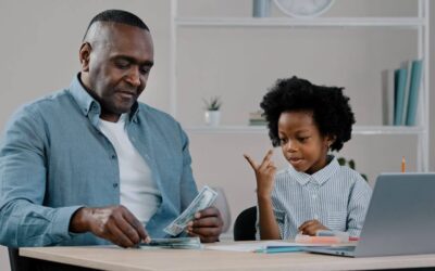 Older man and young granddaughter sit at table counting money